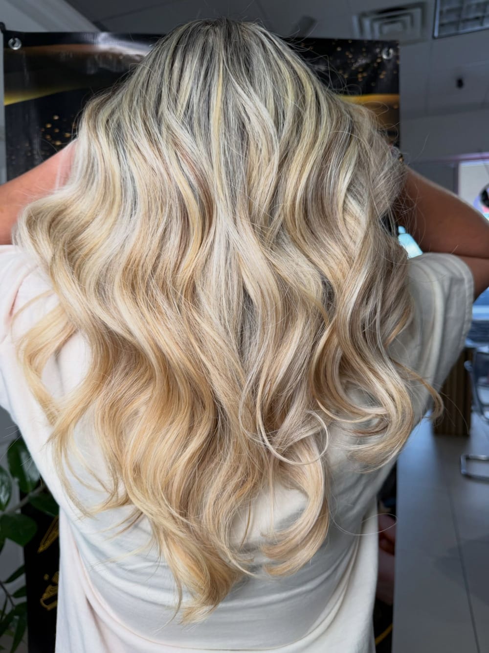 Long honey-blonde balayage in soft waves, seen from behind, done at Paulina’s